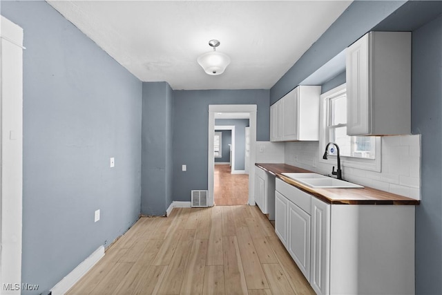 kitchen featuring sink, light hardwood / wood-style flooring, wooden counters, backsplash, and white cabinets