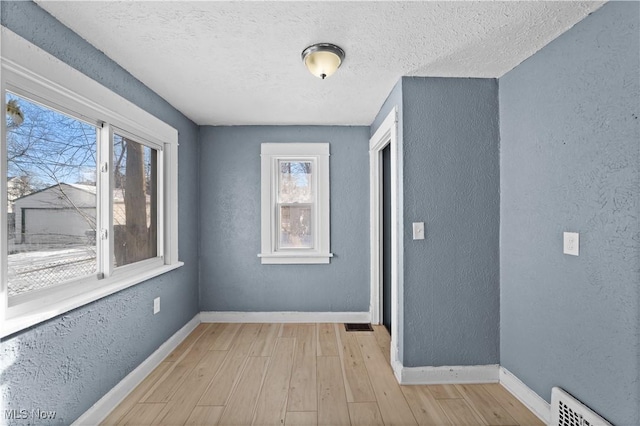 corridor with a healthy amount of sunlight, light hardwood / wood-style floors, and a textured ceiling