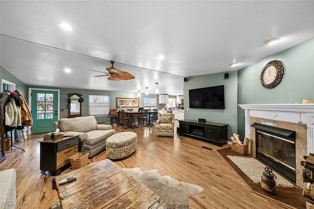 living room with ceiling fan, a tiled fireplace, and light hardwood / wood-style flooring