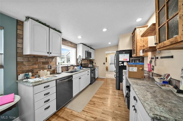 kitchen with decorative backsplash, appliances with stainless steel finishes, sink, white cabinets, and light hardwood / wood-style floors