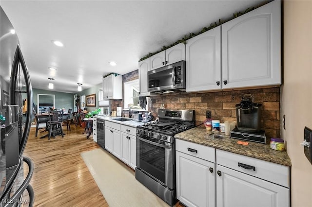 kitchen with white cabinets, light hardwood / wood-style floors, stainless steel appliances, and dark stone counters