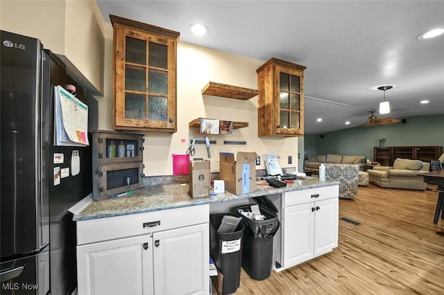 kitchen with white cabinetry, ceiling fan, light stone countertops, light hardwood / wood-style flooring, and black refrigerator