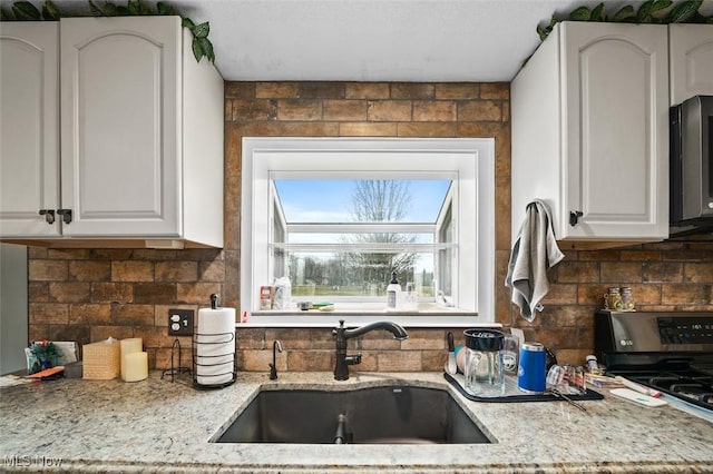 kitchen with tasteful backsplash, white cabinetry, sink, and light stone countertops