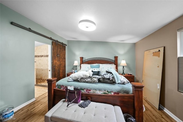 bedroom featuring hardwood / wood-style flooring, ensuite bathroom, and a barn door