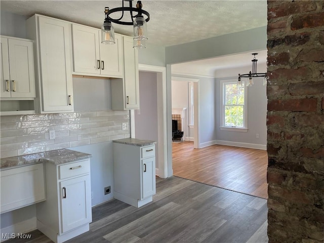 kitchen featuring decorative backsplash, a textured ceiling, wood-type flooring, pendant lighting, and white cabinetry