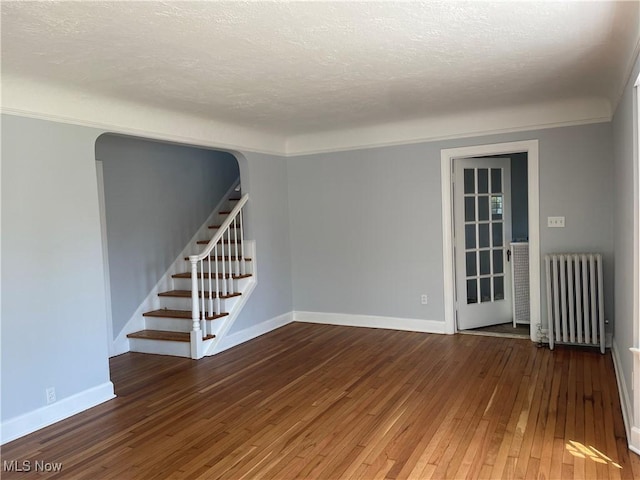 empty room with a textured ceiling, radiator, dark hardwood / wood-style floors, and ornamental molding