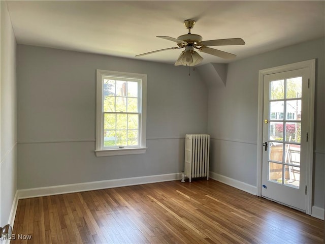 empty room with hardwood / wood-style floors, a wealth of natural light, ceiling fan, and radiator