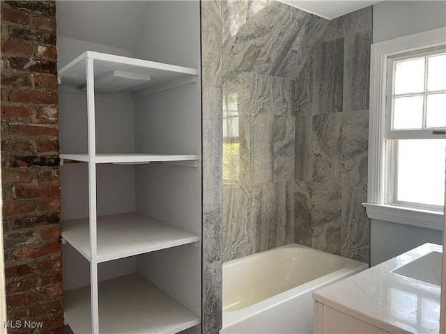 bathroom with vanity, a bathtub, and brick wall