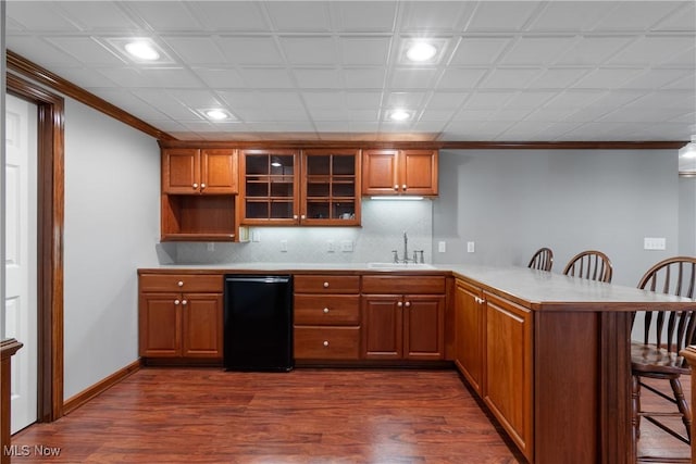 kitchen with sink, dark wood-type flooring, kitchen peninsula, a breakfast bar, and ornamental molding