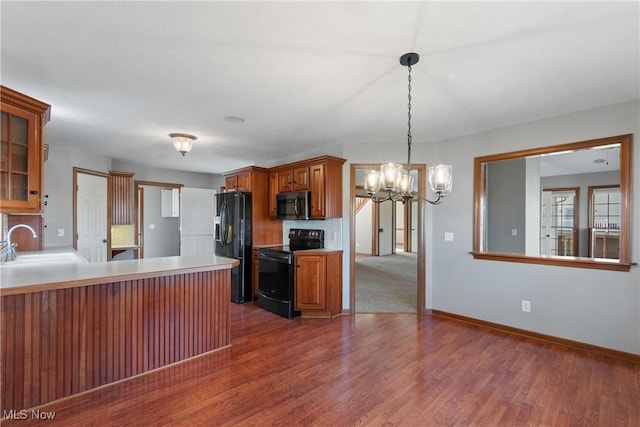 kitchen featuring dark wood-type flooring, sink, black appliances, an inviting chandelier, and hanging light fixtures