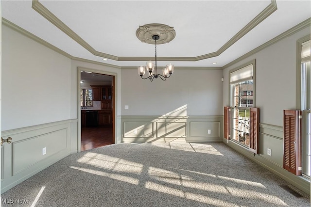 empty room featuring a raised ceiling, carpet floors, crown molding, and a chandelier