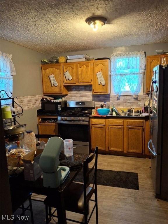 kitchen with tasteful backsplash, stainless steel appliances, a textured ceiling, and light hardwood / wood-style floors