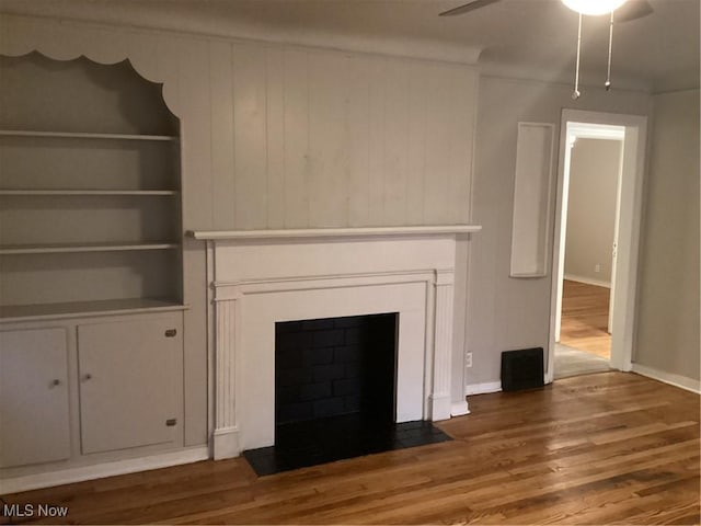 unfurnished living room with built in features, ceiling fan, and dark wood-type flooring