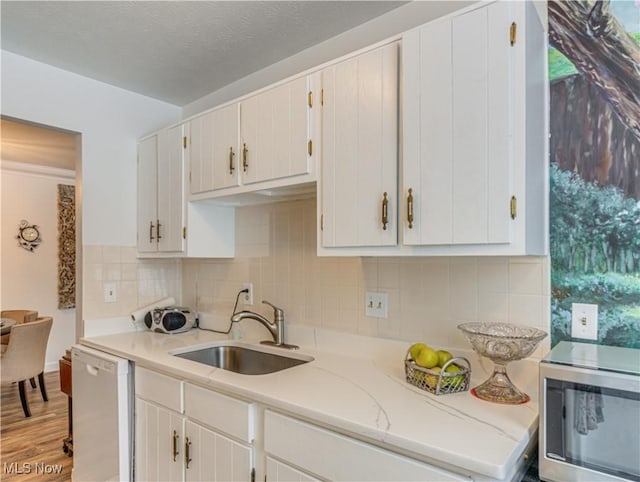 kitchen with white cabinetry, sink, white dishwasher, light stone countertops, and light wood-type flooring