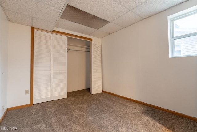 unfurnished bedroom with a paneled ceiling, carpet, and a closet