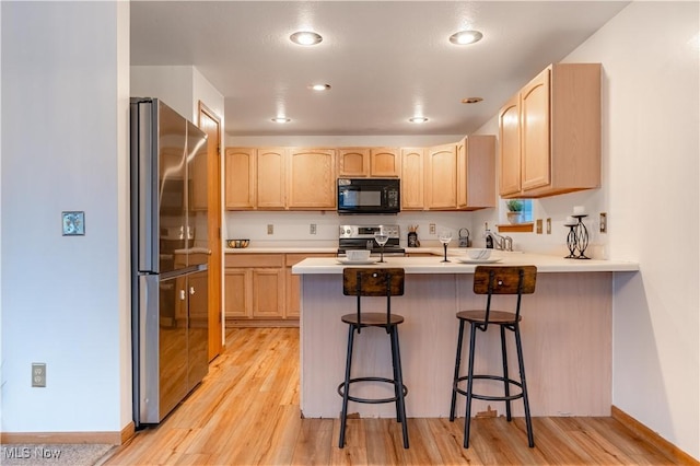 kitchen with a breakfast bar area, light wood-type flooring, light brown cabinetry, kitchen peninsula, and stainless steel appliances