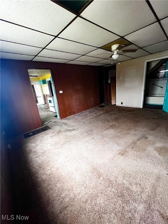 carpeted spare room featuring a paneled ceiling, ceiling fan, and wooden walls