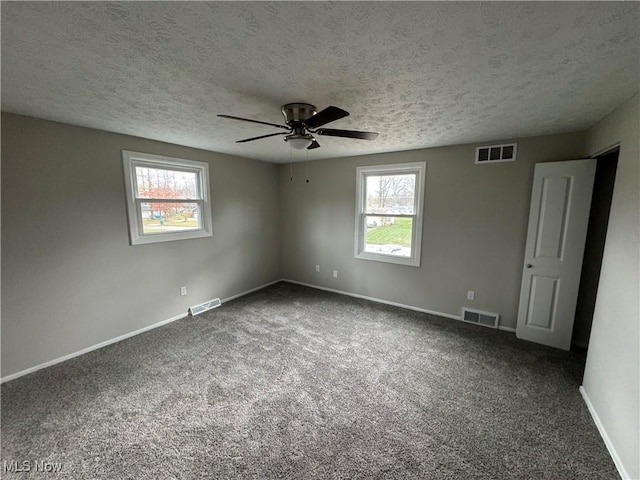 carpeted spare room with a textured ceiling, ceiling fan, and a healthy amount of sunlight