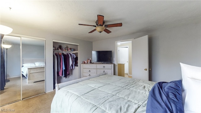 bedroom featuring ceiling fan, light colored carpet, a textured ceiling, and multiple closets