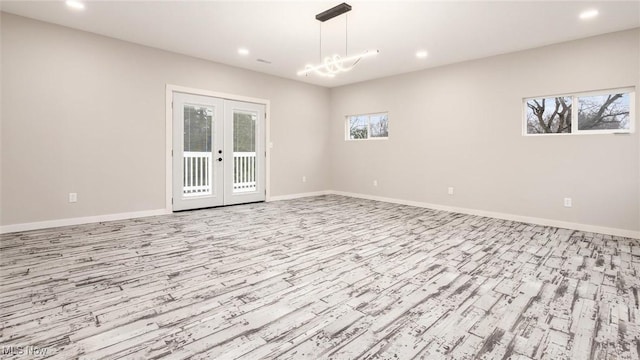 empty room with french doors, light hardwood / wood-style floors, plenty of natural light, and an inviting chandelier