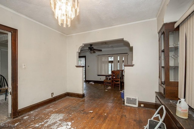 unfurnished dining area featuring a textured ceiling, ceiling fan with notable chandelier, crown molding, and dark wood-type flooring