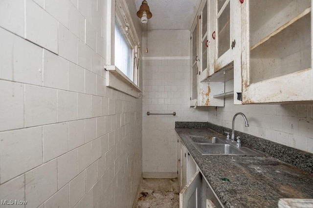 kitchen featuring dark stone countertops, white cabinetry, sink, and tile walls