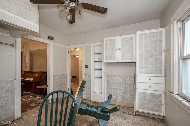 sitting room featuring ceiling fan, tile walls, and a wealth of natural light