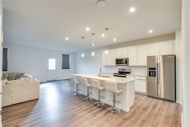 kitchen with appliances with stainless steel finishes, light wood-type flooring, a kitchen island with sink, and sink