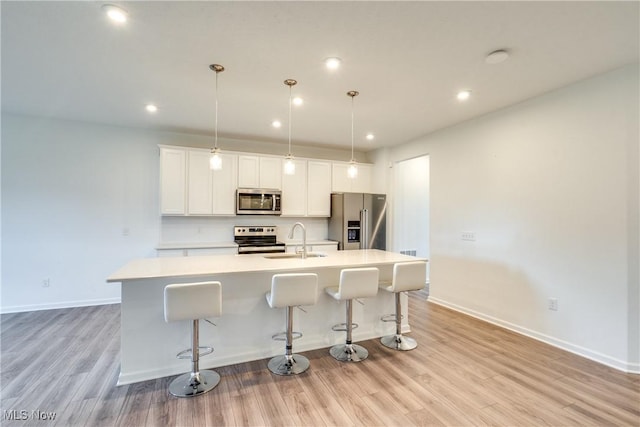 kitchen with pendant lighting, a kitchen island with sink, sink, light wood-type flooring, and appliances with stainless steel finishes