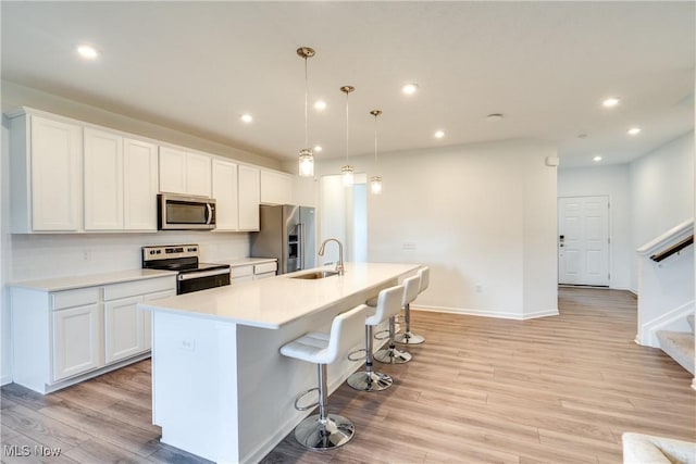 kitchen featuring hanging light fixtures, appliances with stainless steel finishes, an island with sink, white cabinets, and light wood-type flooring