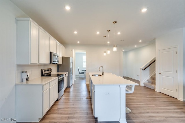 kitchen featuring stainless steel appliances, a kitchen island with sink, light hardwood / wood-style flooring, white cabinets, and hanging light fixtures