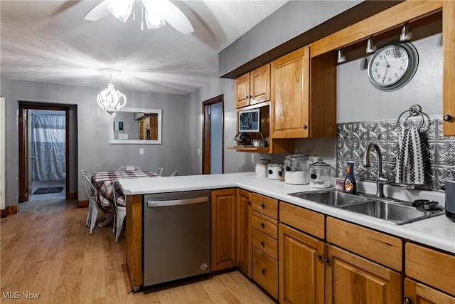 kitchen featuring dishwasher, sink, light hardwood / wood-style flooring, decorative light fixtures, and kitchen peninsula