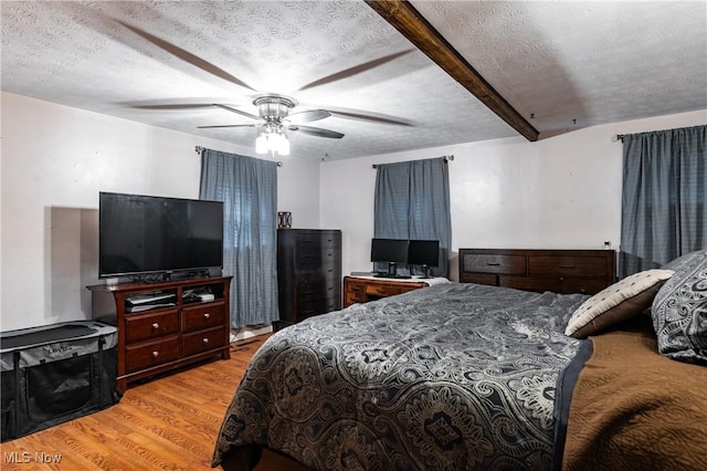 bedroom featuring a textured ceiling, light wood-type flooring, ceiling fan, and beam ceiling