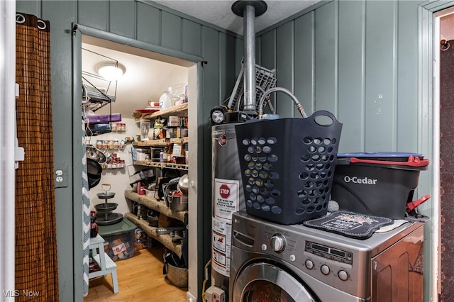 clothes washing area featuring washer / clothes dryer, water heater, light hardwood / wood-style floors, and a textured ceiling