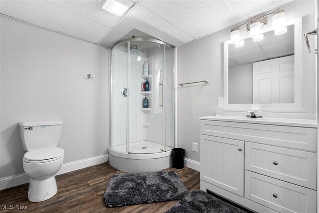 bathroom featuring a stall shower, a drop ceiling, wood finished floors, and baseboards