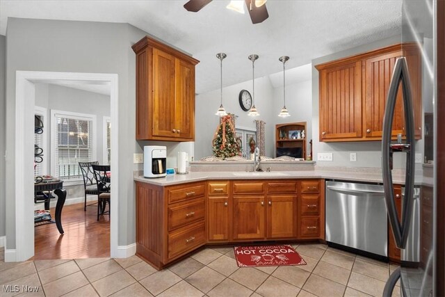 kitchen with a sink, brown cabinets, stainless steel appliances, light tile patterned flooring, and light countertops