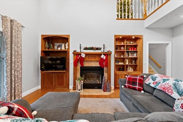 living area featuring a towering ceiling, a fireplace with flush hearth, wood finished floors, and baseboards