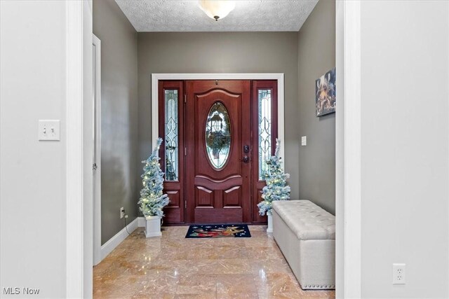 entrance foyer featuring a textured ceiling, marble finish floor, and baseboards