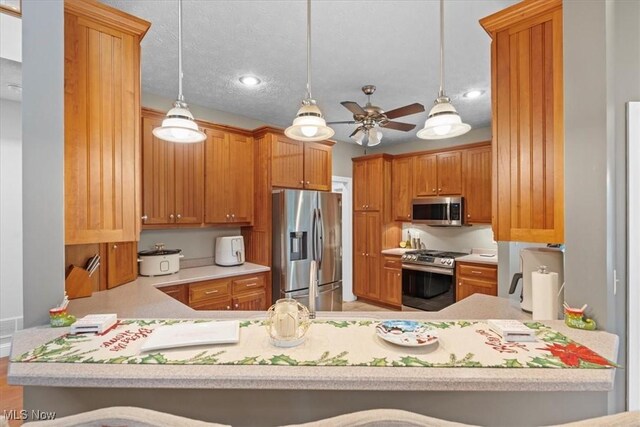 kitchen featuring appliances with stainless steel finishes, a peninsula, a ceiling fan, and hanging light fixtures
