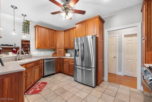kitchen featuring brown cabinetry, light tile patterned floors, appliances with stainless steel finishes, light countertops, and a sink