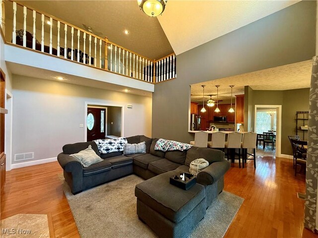 living area featuring a towering ceiling, visible vents, light wood-style flooring, and baseboards