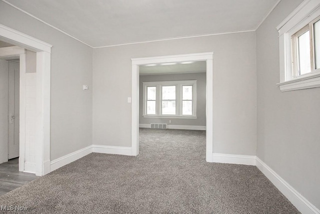 spare room with dark colored carpet, a healthy amount of sunlight, and crown molding