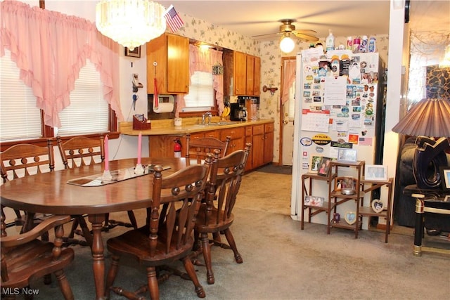 dining space with ceiling fan with notable chandelier, light colored carpet, and sink