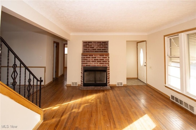 unfurnished living room featuring wood-type flooring, a textured ceiling, and a brick fireplace