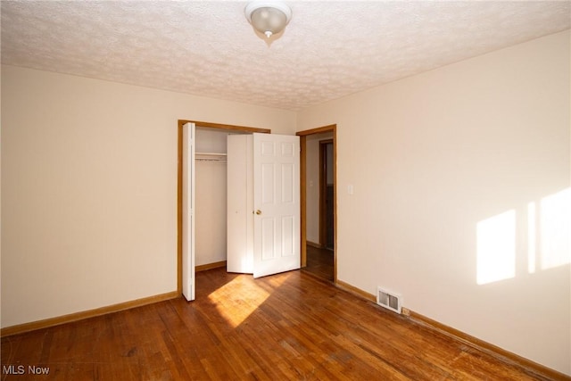 unfurnished bedroom featuring a textured ceiling, dark wood-type flooring, and a closet