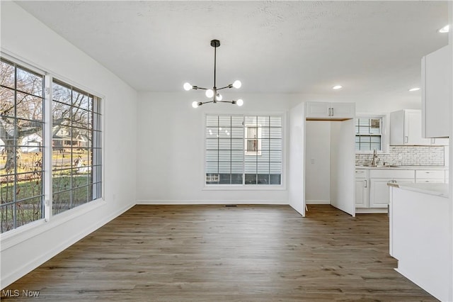 unfurnished dining area with sink, dark wood-type flooring, and an inviting chandelier