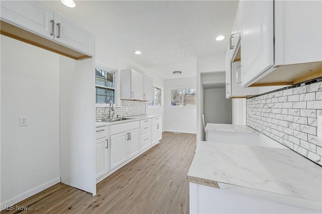 kitchen with backsplash, light hardwood / wood-style flooring, white cabinetry, and sink