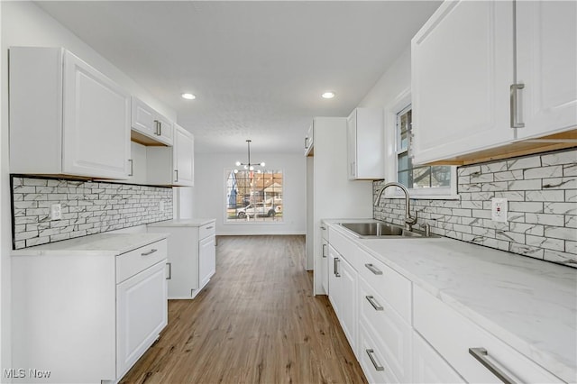 kitchen with white cabinets, light wood-type flooring, decorative light fixtures, and sink