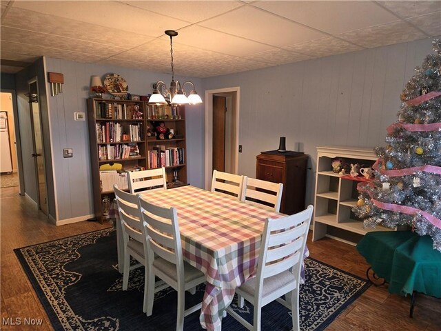 dining room featuring wood walls, dark hardwood / wood-style floors, and an inviting chandelier