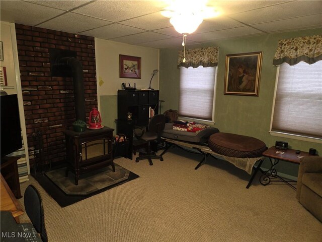 living area with carpet, a paneled ceiling, a wood stove, and a healthy amount of sunlight